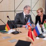 delegaci międzykulturowi omawiają punkty przemówienia kolegi, wieloetniczne spotkanie w nowoczesnej sali konferencyjnej, wszyscy w strojach formalnych, dzielenie się opiniami