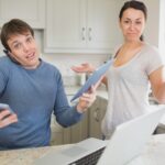 Zajęty człowiek za pomocą dwóch tabletek i laptopa z żoną trzymając się za ręce przesłuchanie