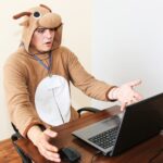 Pracownik biurowy w stroju cosplay krowy. Facet w zabawnej piżamie zwierzęcej w pobliżu laptopa. Parodia menedżera.