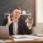 Szczęśliwy księgowy pokazujący kalkulator i znak ok w swoim miejscu pracy. Wzrost dochodów, odpowiednia koncepcja strategii marketingowej