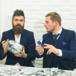 Koncepcja kwestii gotówkowych. Koledzy zbierają pieniądze w słoiku zamiast na konto bankowe. Partnerzy biznesowi, biznesmeni na spotkaniu w biurze. Menedżer z brodą i kolega ze słojem gotówki i karty