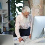Starszy biznesmen ze stylową brodą pracuje na laptopie przy biurku w biurze