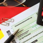 Niemiecki formularz zwrotu podatku dochodowego z długopisem i europejskimi banknotami euro leżą na fladze z bliska Podatnicy w Niemczech używający waluty euro do płacenia podatków