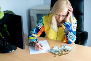 Zamyślona kobieta w średnim wieku licząca pieniądze w euro i robiąca notatki przy biurku w domowym biurze