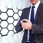 Skoncentrowany biznesmen wysyłający SMS-y na swoim telefonie komórkowym przeciwko sześciokątnemu pokojowi