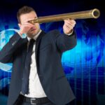 Biznesmen patrzeje przez teleskop przeciw globalnej biznesowej grafice w błękicie