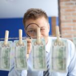 Mężczyzna patrzy przez szkło powiększające na banknoty studolarowe wiszące na spinaczach do bielizny